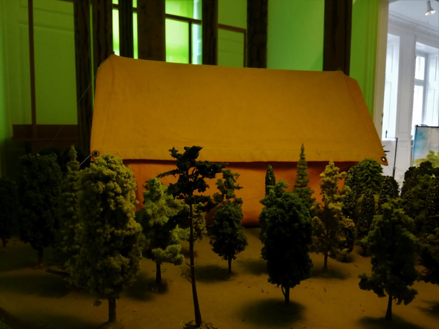 “Ventesals-maleri – Installation til galleriets sidste stue” 2022. Træ, lister, stof, skumgummi, papir og arvede modeljernbanetræer.